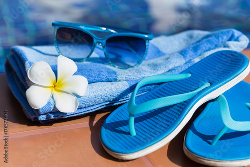 Blue slippers, sunglasses and towel on border of a swimming pool