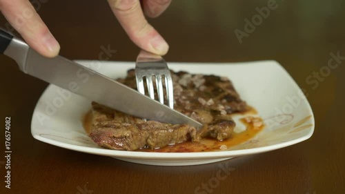 Close up locked shot of steak. Hands with knife and fork take part of meat steak from plate. photo
