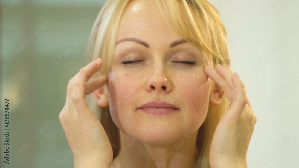 Blonde with closed eyes massaging her face with her fingers
