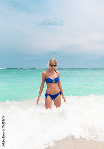 Young pretty blond woman in blue bikini on white tropic beach