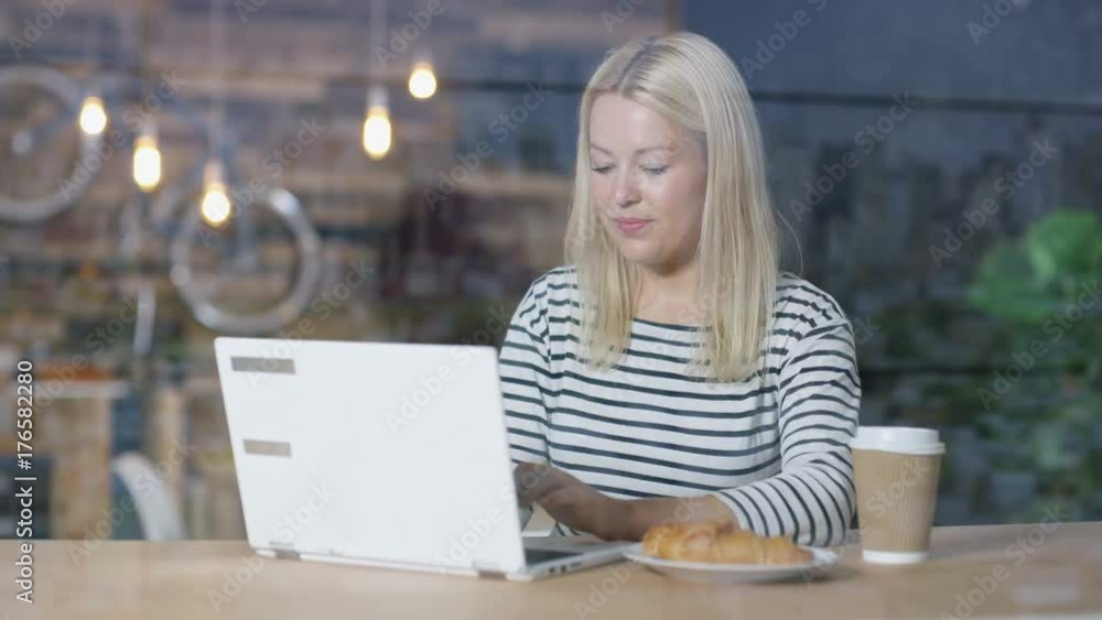 Young woman using laptop in a cafe with coffee & croissant Young woman using laptop in a cafe with coffee & croissant
