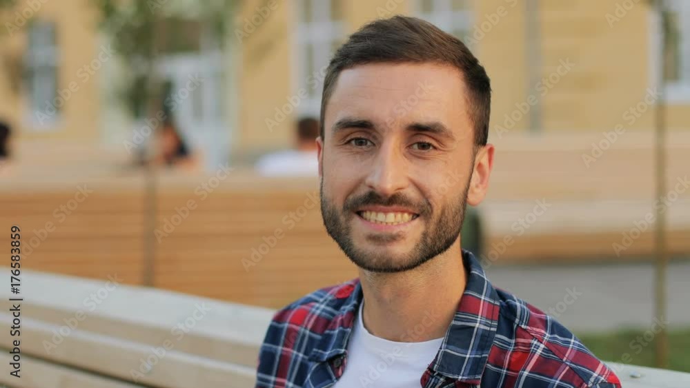 A close up portrait of a handsome young man sitting on the bench and smiling into the camera A close up portrait of a handsome young man sitting on the bench and smiling into the camera