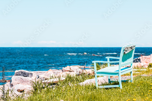 One peaceful blue aquamarine turquoise green beach chair empty bench in front of ocean