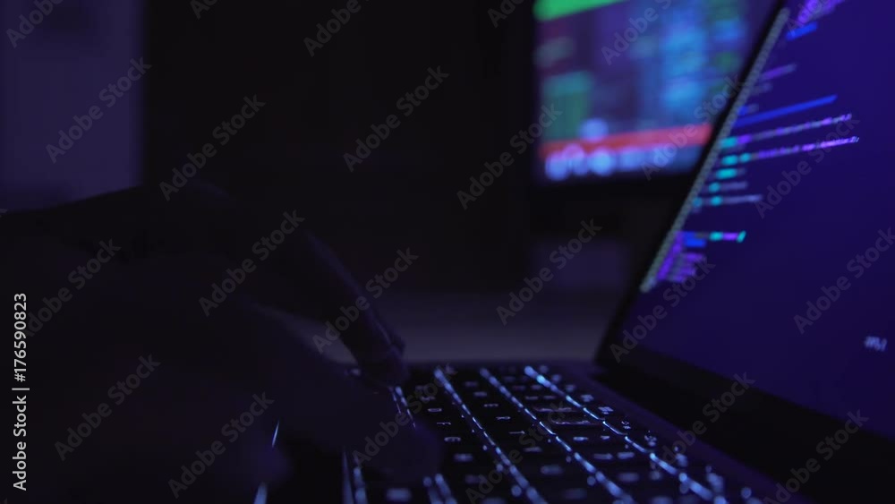 Male hacker working on a computer in a dark office room. Male hacker working on a computer in a dark office room.