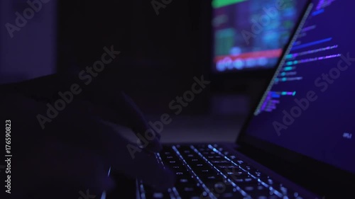 Male hacker working on a computer in a dark office room.
