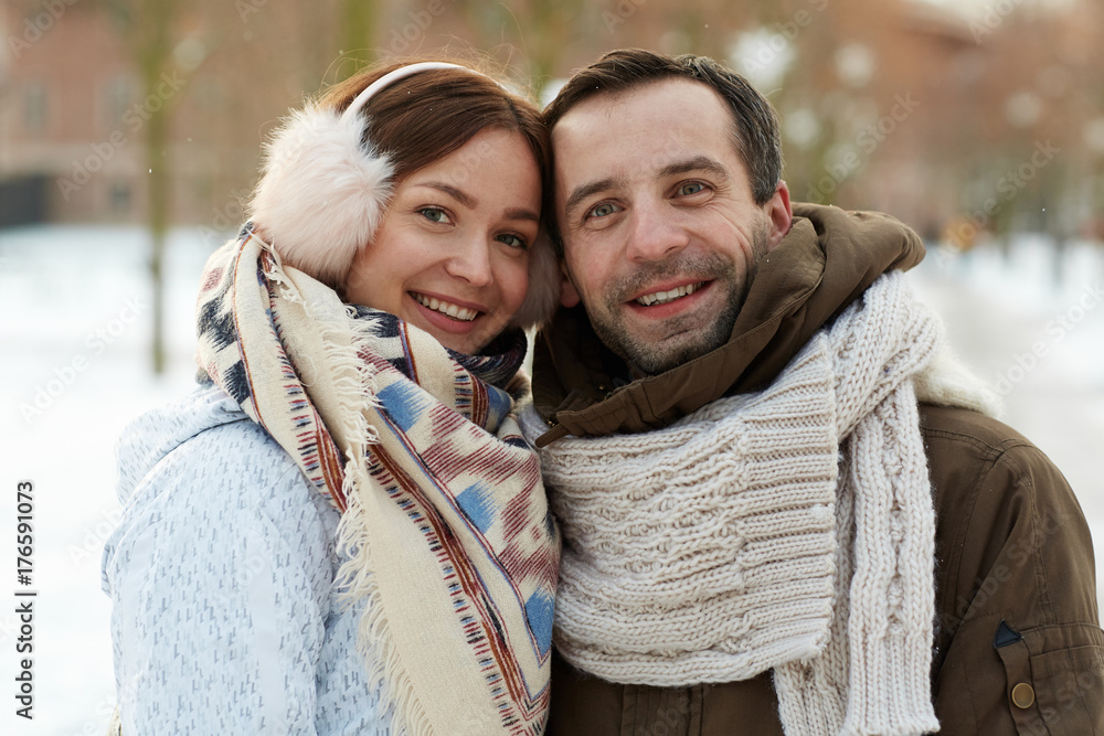 Happy amorous couple in winterwear looking at camera in natural environment