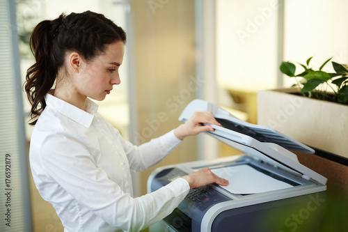 Young secretary making photocopies on xerox machine in office photo