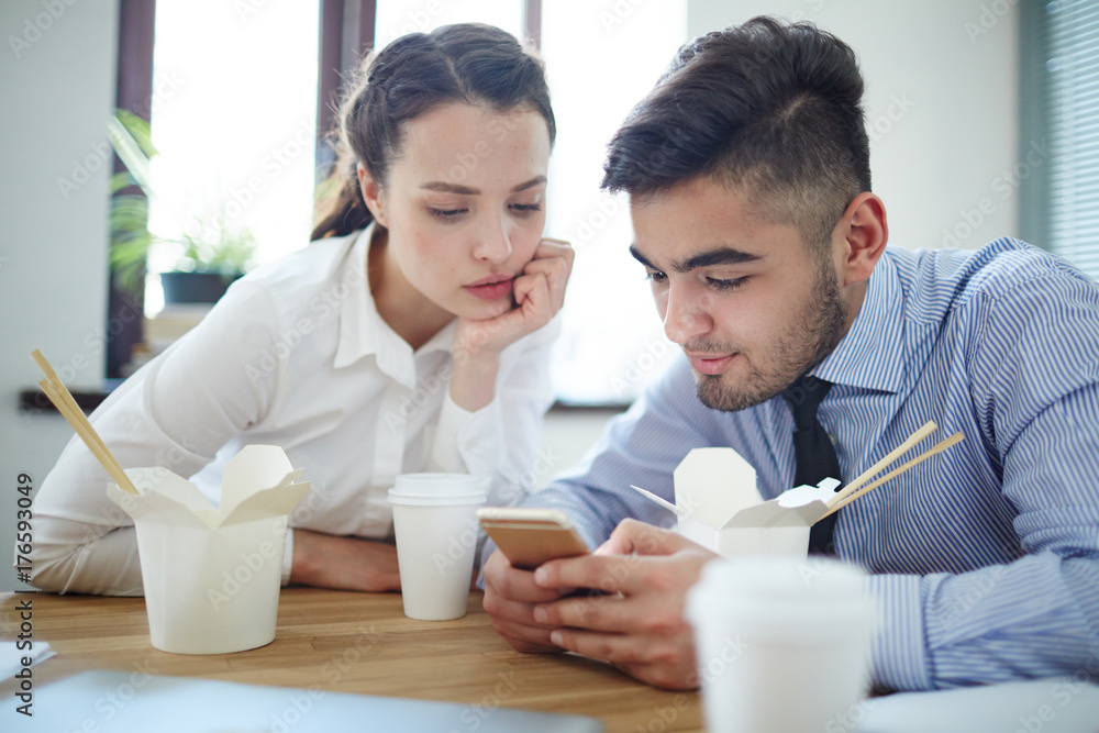 Attentive co-workers waching curious things in smartphone net at lunch break Attentive co-workers waching curious things in smartphone net at lunch break