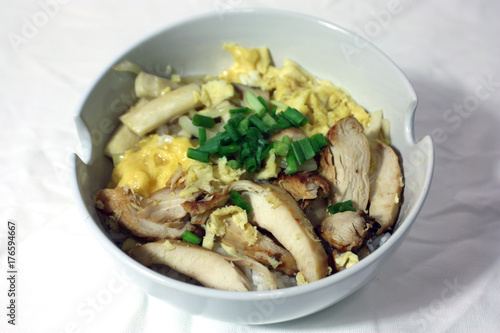 Baked chicken with eggs and mushrooms, topped with onion on the rice in the white bowl, on the white fabric. Fusion food of perfumed chicken and eggs with rice in the whiter container of food.