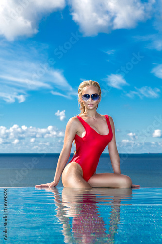 Beautiful blonde woman model with wet hair and elegant makeup sitting in a pool with amazing views in a luxury hotel, wearing jewelry, earrings with the crystals and wet naked body photo