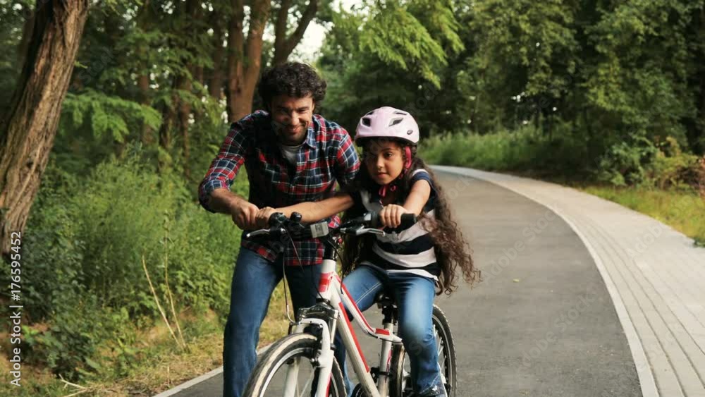 Closeup. Portrait of a little girl and her father. Dad teaching his daughter to ride a bike. He lets her go. Moving camera. Blurred background Closeup. Portrait of a little girl and her father. Dad teaching his daughter to ride a bike. He lets her go. Moving camera. Blurred background