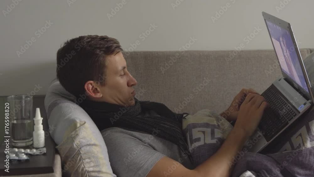 sick young man in bed working on notebook. Plenty pills and medications are on the bedside table. sick young man in bed working on notebook. Plenty pills and medications are on the bedside table.