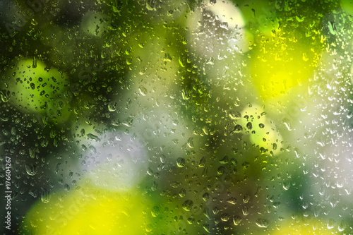 Rain drop on window glass with bright green and white blur bokeh abstract light spring forest background.