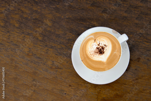 Top view of hot cappuccino coffee with heart shaped froth on classic wood table sprinkled coffee powder

