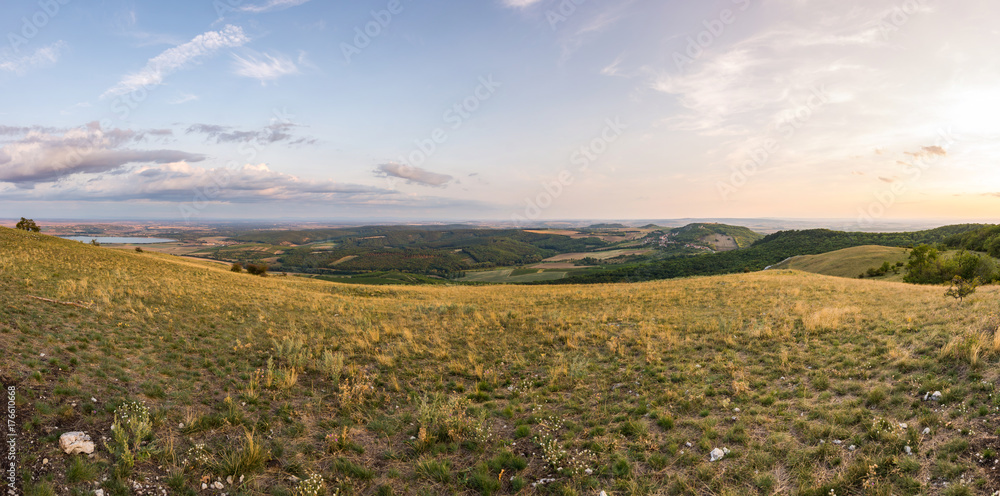 Sunset landscape panorama, hills in golden hour, small village in valley, beautiful colors and clouds.