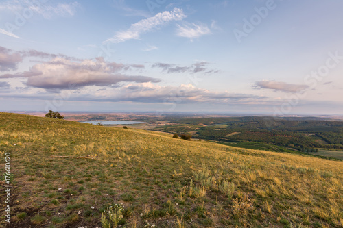 Sunset landscape panorama, hills in golden hour, small village in valley, beautiful colors and clouds.