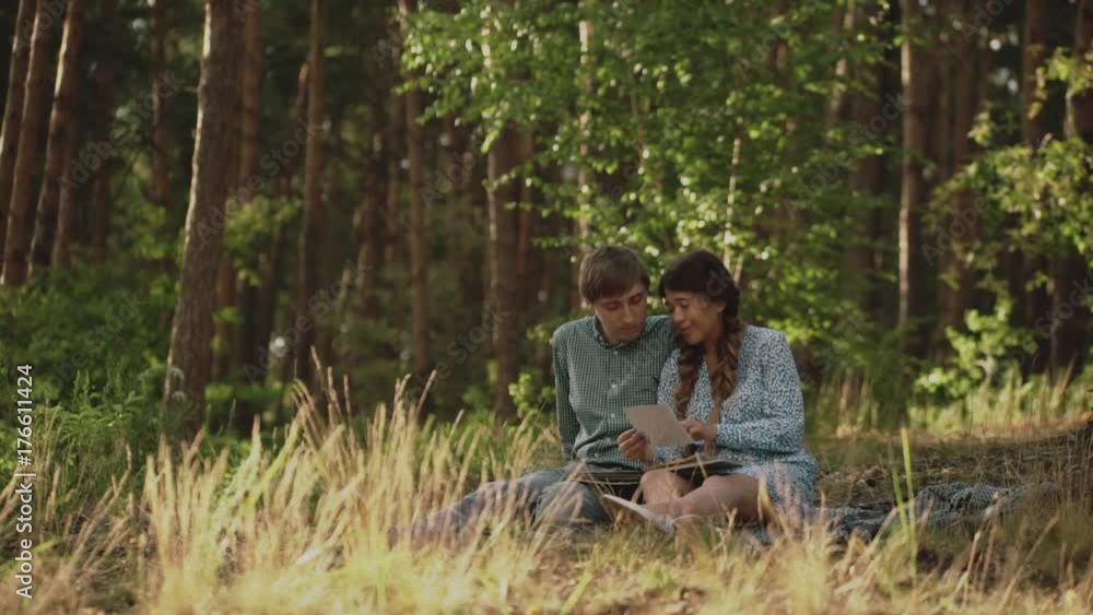 Couple sitting in picnic in the sunset forest. Family looking at their photo album sitting in the park. Happy couple with photo album.A young attractive couple walking through the forest with their Couple sitting in picnic in the sunset forest. Family looking at their photo album sitting in the park. Happy couple with photo album.A young attractive couple walking through the forest with their
