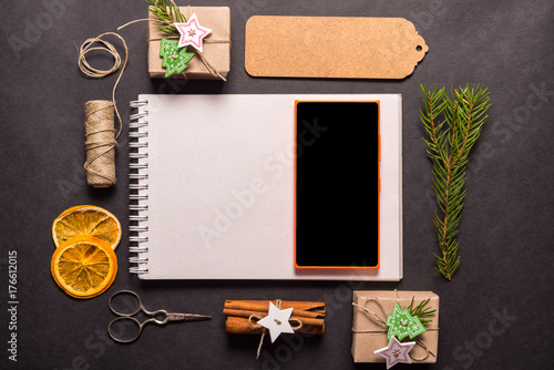 Fototapeta Naklejka Na Ścianę i Meble -  Spiral notebook and smart phone on black background, Christmas concept