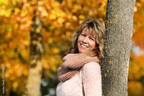 Happy mature woman leaning against a tree in front of autumn leaves photo