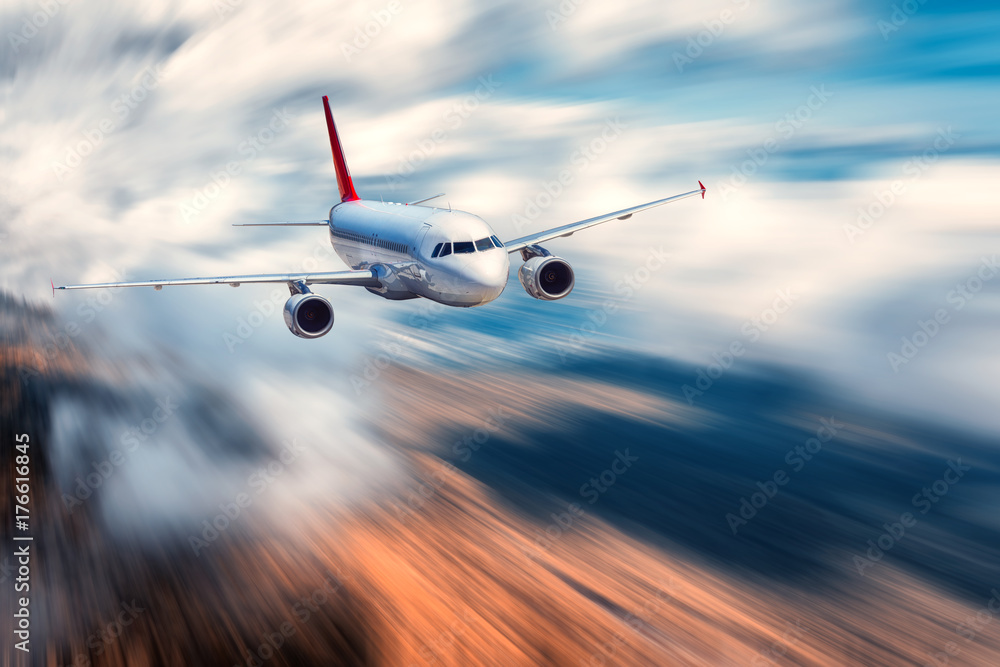 Fototapeta premium Airplane with motion blur effect. Landscape with flying passenger airplane and blurred background with sky with low clouds, orange forest at sunset. Passenger airplane is landing. Commercial aircraft