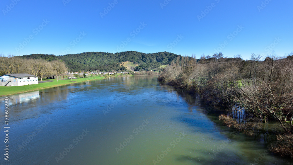 River flowing alongside a village with low hills in the background