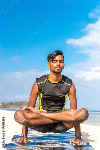 Asian yoga man practice yoga on the beach with a clear blue sky background. Yogi on the tropical beach of Bali island, Indonesia. © belart84