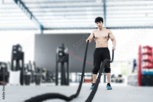 young man execute exercise in fitness center. male athlete training with battle rope in gym. sporty guy working out in health club.