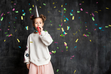 Little fashionable girl having fun at the birthday party on the background of a school board and confetti
