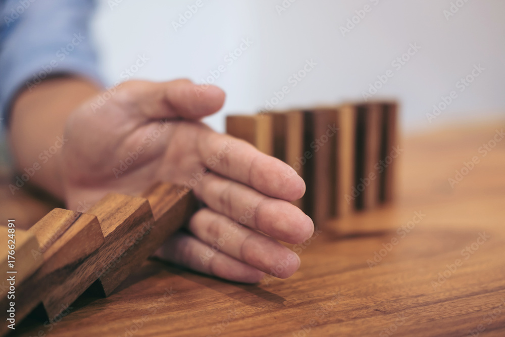 Risk and strategy in business, Close up of businessman hand stopping wooden block from falling in the line of domino