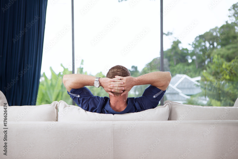 portrait of young man with hands behind his head is relaxing on couch