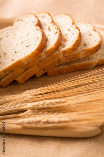 Wheat Bread Slices on a Cutting Board with Wheat. a side angle shot of slices of wheat bread angled on a cutting board with wheat in the foreground