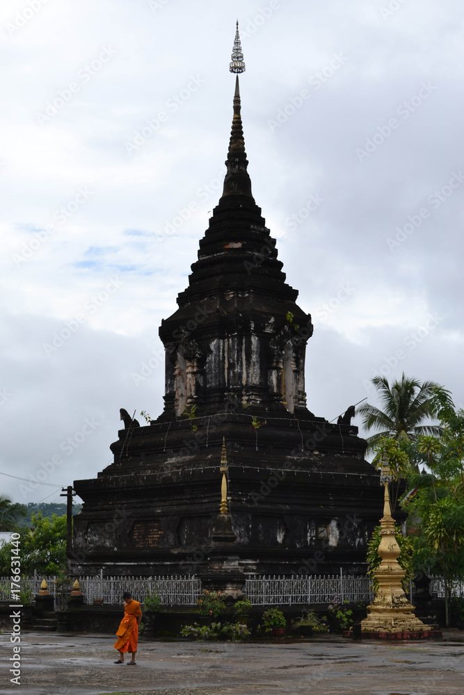 A young Buddhist monk walking in front of one stupa in Luang Prabang, Laos