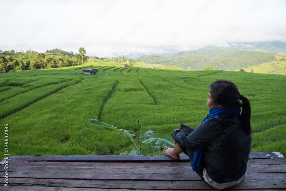 Woman tourism sitting on wood balcony to see view of green rice fields on terraces in Thailand at Ban Pa Pong Pieng in Mae chaem, Chaing Mai.
