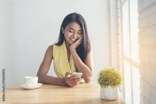 Young asian woman using smart phone while sitting by window cafe background, People technology and lifestyle