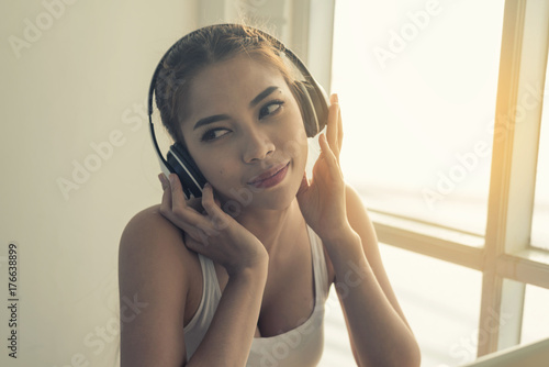 Asian women listen to music with wireless headphones by the window.