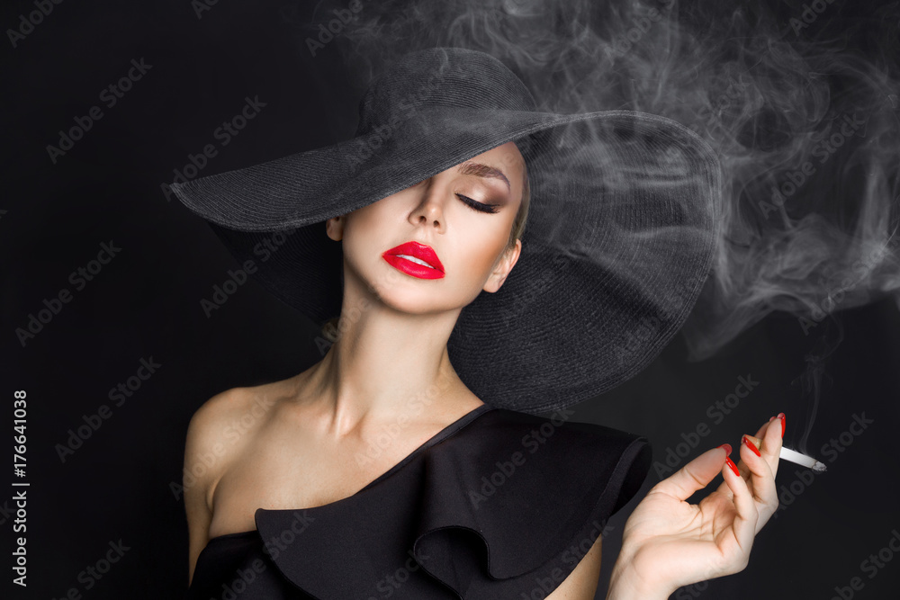 Elegant woman, femme fatale in black hat with cigarette in hand. On black  background Stock Photo | Adobe Stock
