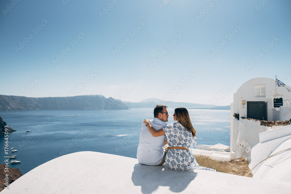 The couple is sitting on the roof in Santorini, hugging and laughing