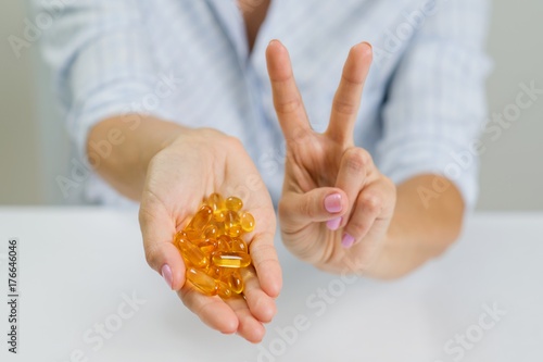 Hands of a woman holding fish oil Omega-3 capsules and showing v