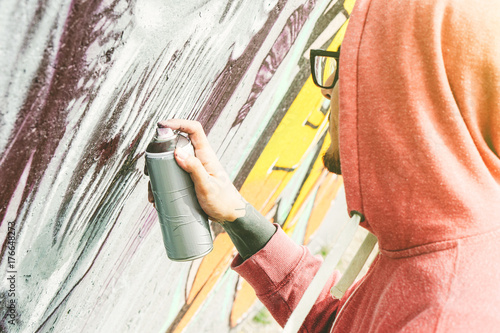 Street artist painting graffiti with color spray his art on the wall - Young man writing and drawing murales on the street - Urban lifestyle and contemporary art concept