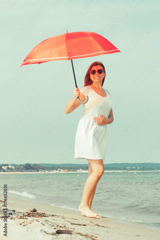 Redhead woman walking on beach holding umbrella Redhead woman walking on beach holding umbrella