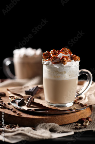 Fototapeta Naklejka Na Ścianę i Meble -  Composition with two glass of cappuccino topped with whipped cream and served with coffee beans and chocolate on wooden chopping board over black background