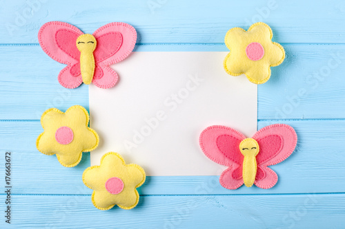 Craft pink and yellow butterfly and flowers with white paper, copyspace on blue wooden background. Hand made felt toys. Abstract sky.