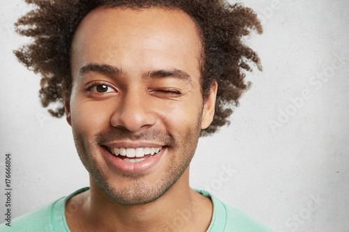 Foto Extreme close up of mixed race handsome man has trendy hairdo, smiles pleasantly and blinks eye, flirts with girlfriend