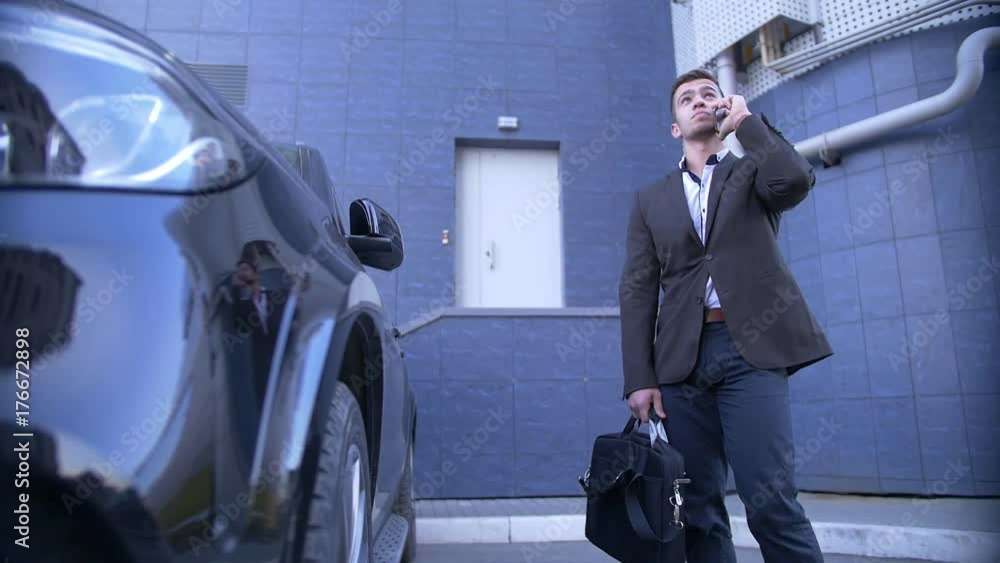 Young perspective businessman talk on mobile, stands beside with fashionable car Young perspective businessman talk on mobile, stands beside with fashionable car