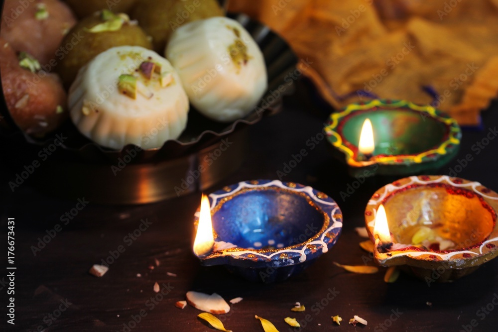Colorful Clay  Diya lamps lit with sweets on side - Happy Diwali, selective focus