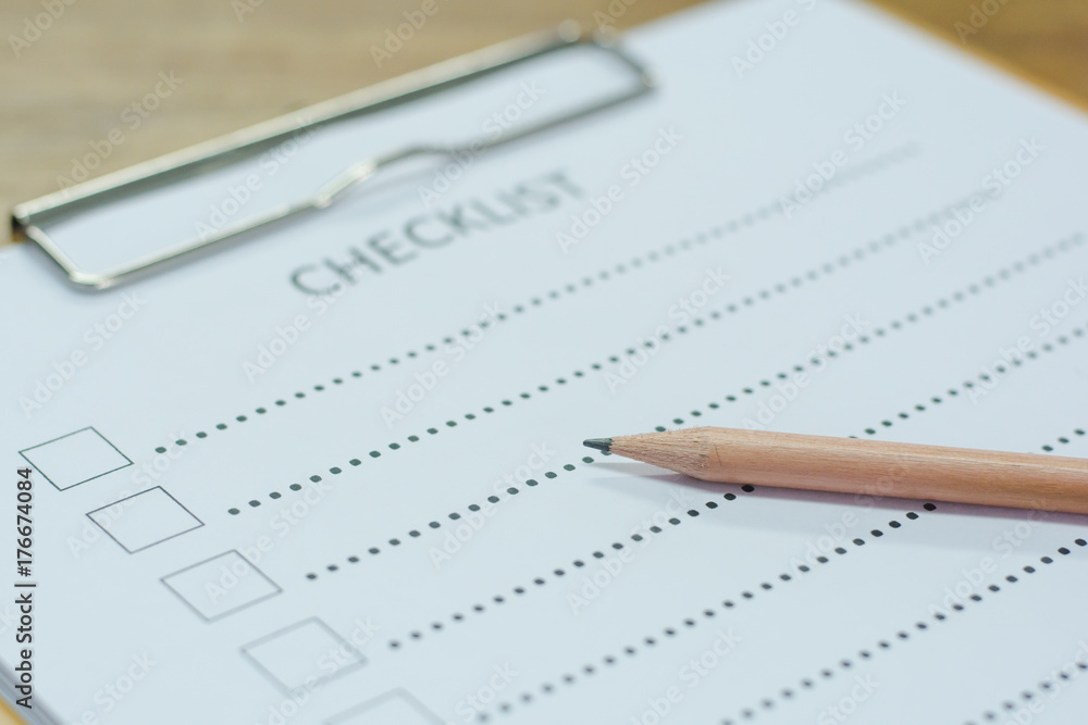 Checklist concept - checklist, paper and a pen with checklist word on wooden table Checklist concept - checklist, paper and a pen with checklist word on wooden table