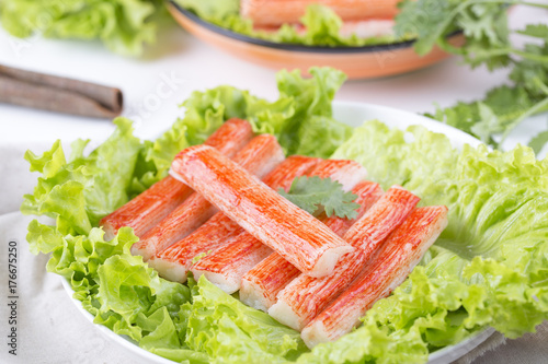 Red crab stick in a white plate. And green lettuce and coriander, pepper and other spices. 
