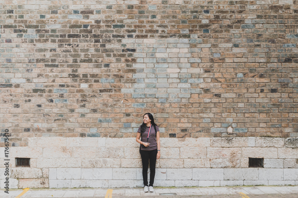 Young beautiful Asian woman are traveling and standing on the road with old brick wall background.Journey and wanderlust lifestyle concept. Young beautiful Asian woman are traveling and standing on the road with old brick wall background.Journey and wanderlust lifestyle concept.