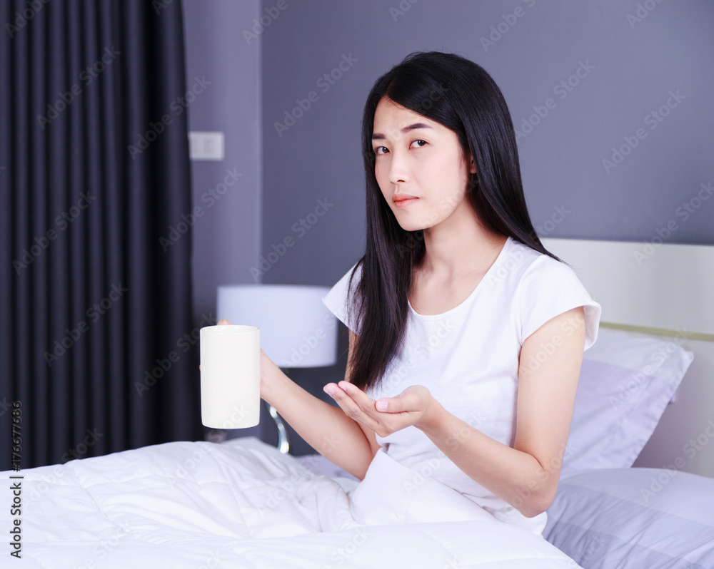 Woman taking pills and drink of water on bed in bedroom Woman taking pills and drink of water on bed in bedroom