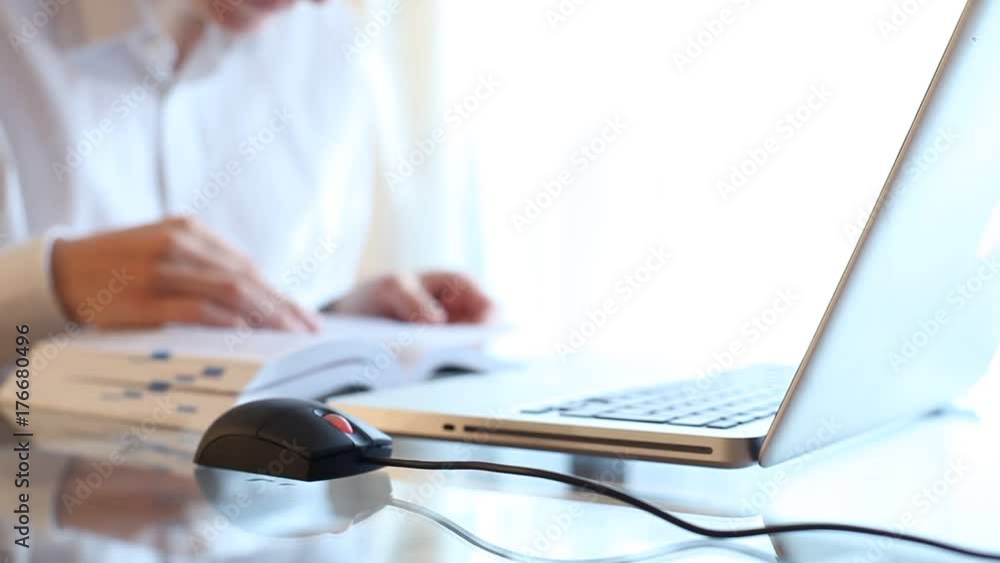 Woman using laptop mouse and searching in a book Woman using laptop mouse and searching in a book